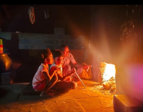 Children and village elder sitting beside a glowing traditional wood-fired hearth during the cultural immersion evening